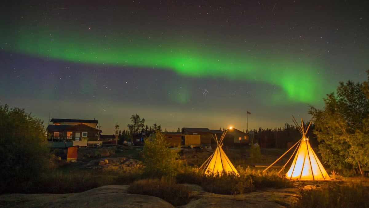 Beautiful Northern Lights illuminating a campsite with tipis in Yellowknife, Canada, at night.